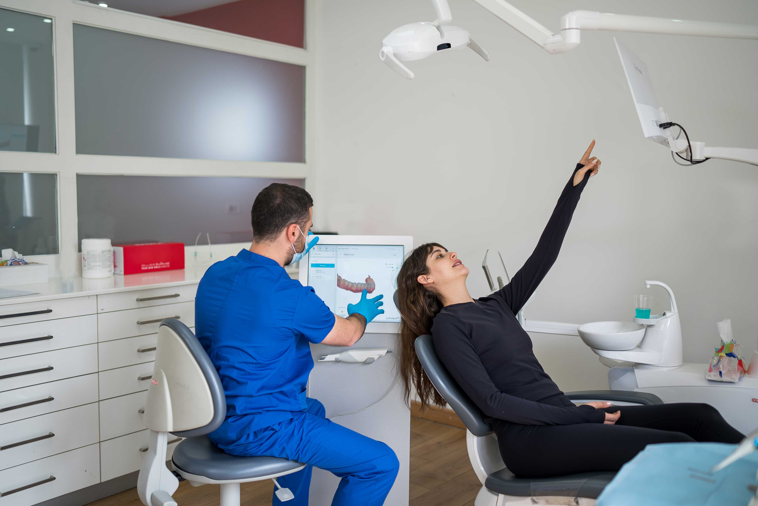 طبيب أسنان يجري مسحاً لأسنان المريض في عيادة متخصصة ويظهر شكل الأسنان على شاشة صغيرة في الخلف